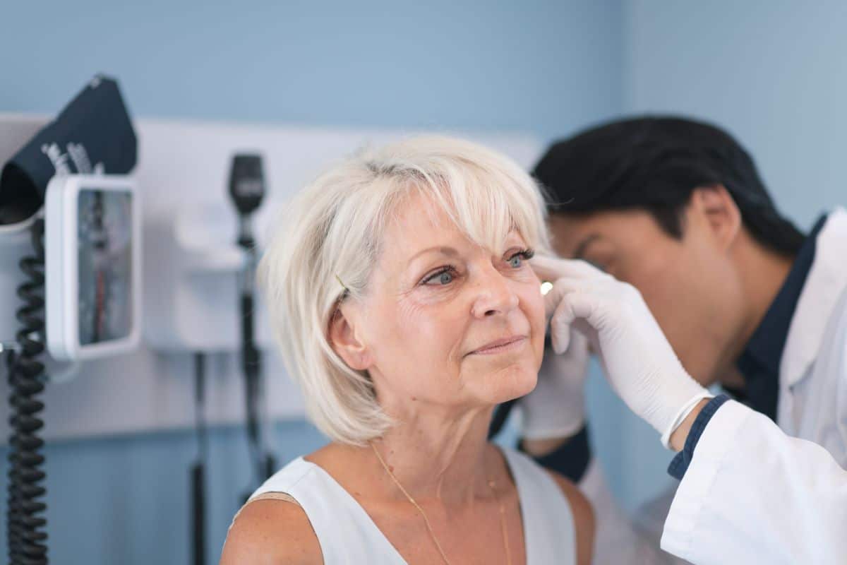 male doctor looking older female patients ear for indications of an ear infection