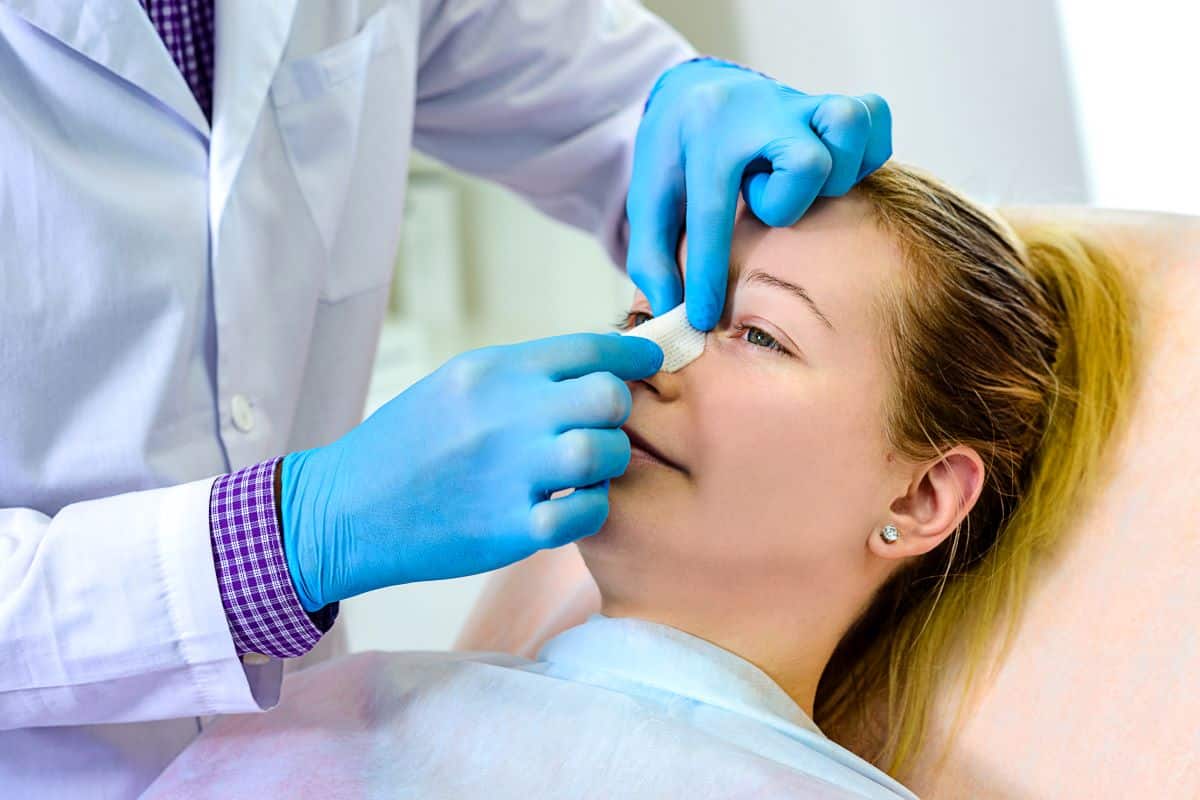 Nasal-Fractures doctor wearing blue rubber gloves is placing a bandage over the bridge of a female patients nose
